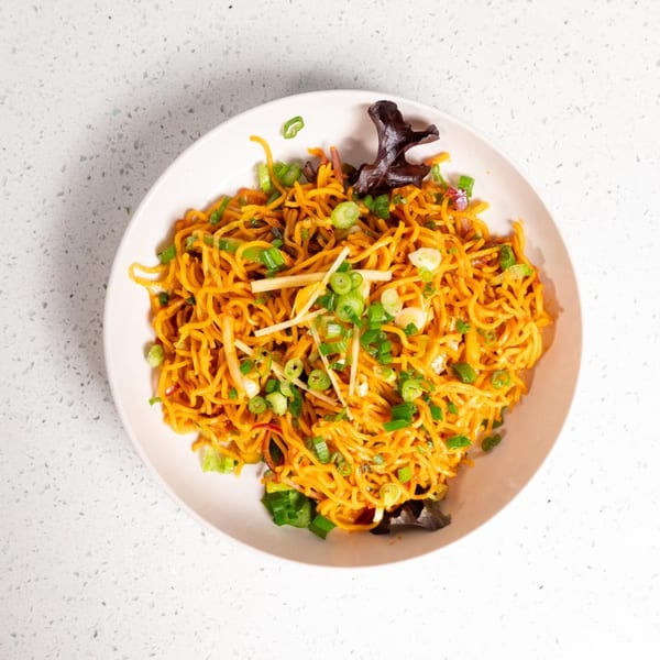 Gulab Indian Bistro's orange noodles with green onions and ginger in a white bowl.
