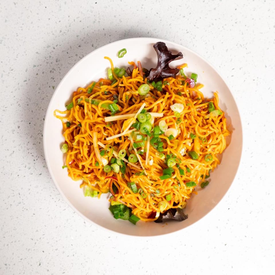 Gulab Indian Bistro's orange noodles with green onions and ginger in a white bowl.