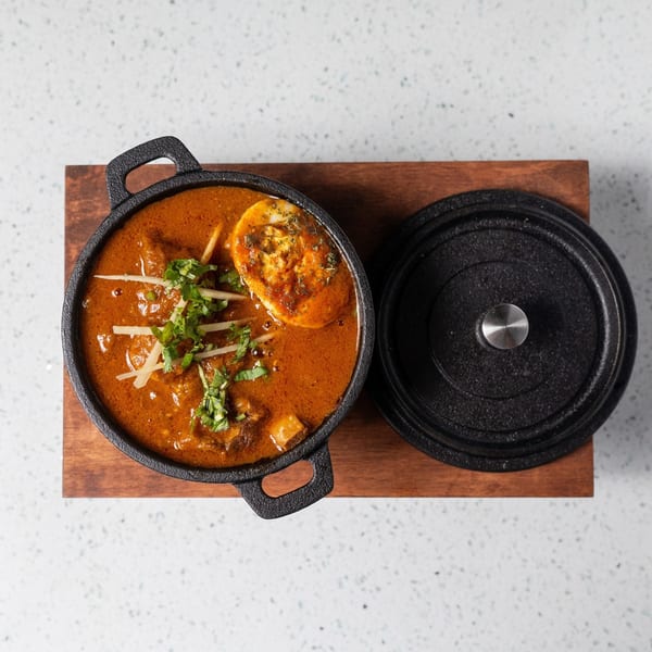 Gulab Indian Bistro's Indian curry with egg, garnished with cilantro and ginger, in a black pot.