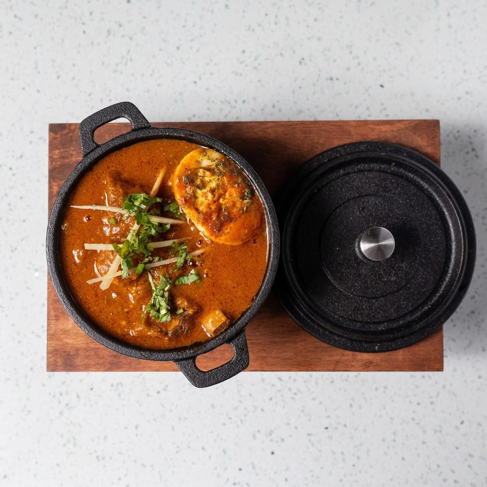 Gulab Indian Bistro's Indian curry with egg, garnished with cilantro and ginger, in a black pot.