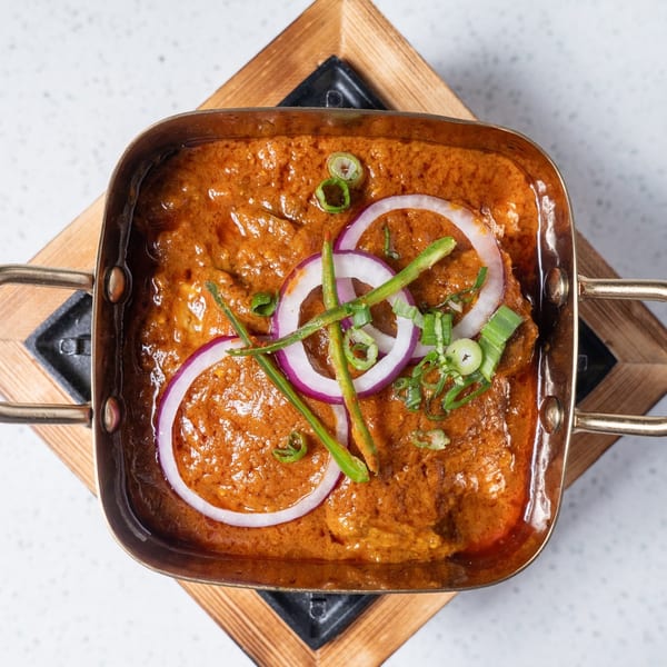 Overhead view of a Gulab Indian Bistro curry dish, garnished with red onion and green chilies.