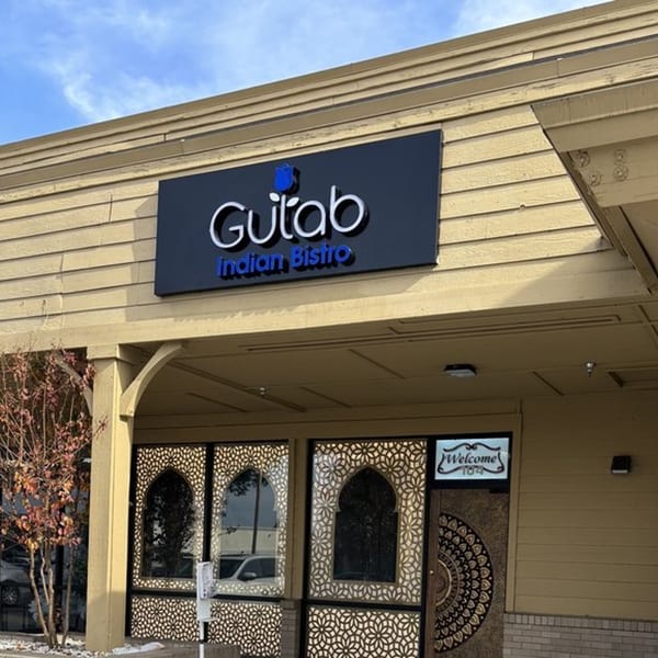 Exterior of Gulab Indian Bistro with a black sign, ornate windows, and a 'Welcome' sign.