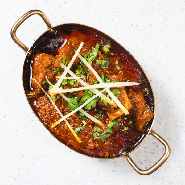 Gulab Indian Bistro's rich, red curry with paneer and cilantro in a brass serving dish.