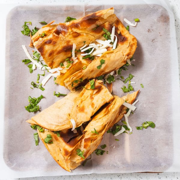 Two golden-brown Indian parathas, folded and topped with fresh cilantro and shredded cheese.