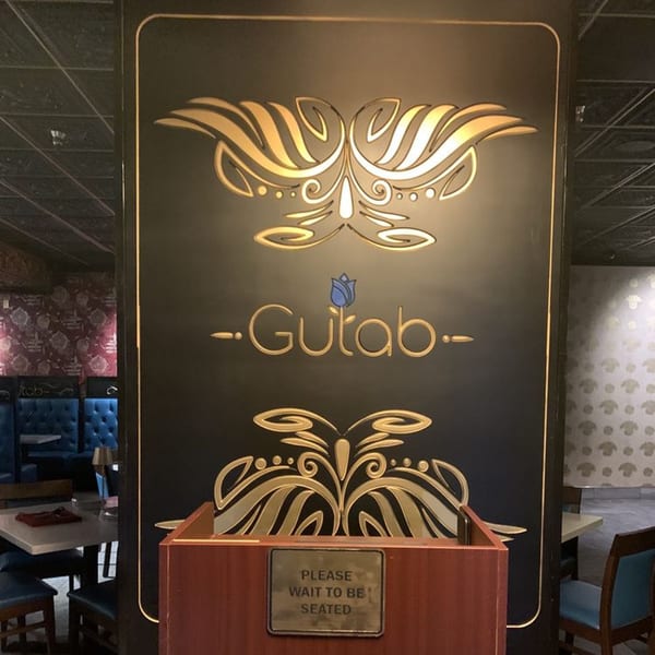 Gulab Indian Bistro's ornate black and gold entrance sign with a "Please Wait to Be Seated" stand.