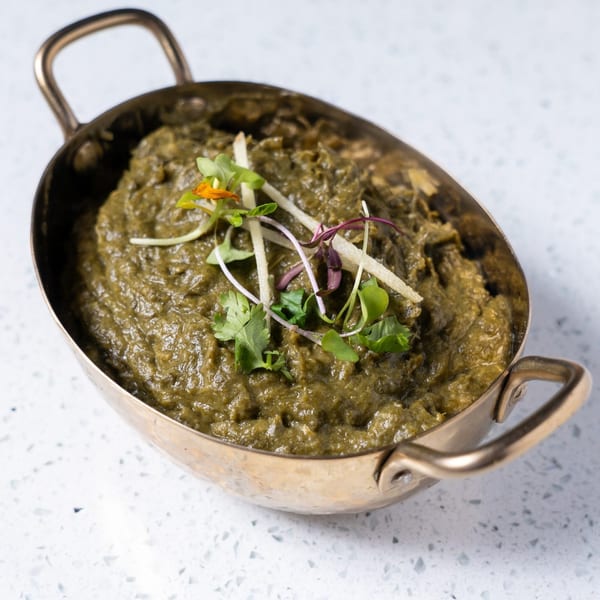 Gulab Indian Bistro's vibrant green Saag, garnished with fresh herbs, in a brass serving bowl.
