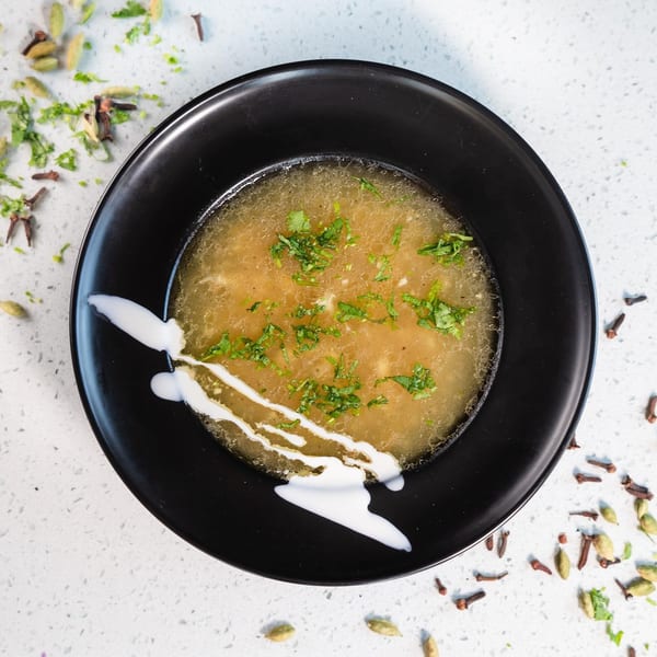 Overhead view of Gulab Indian Bistro's chicken soup, garnished with cilantro and cream, on a black plate.